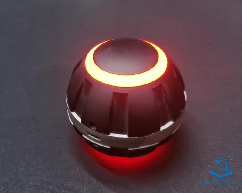 May include: A black and silver round object with a glowing orange ring around the top and a red light emanating from the bottom.