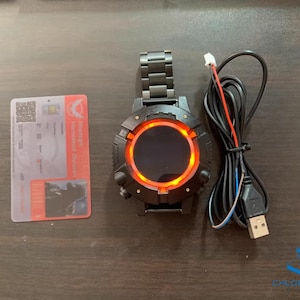 May include: A black smartwatch with a red ring around the screen. The watch is connected to a charging cable.