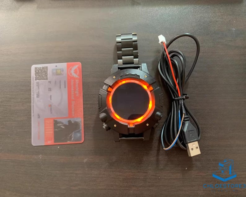 May include: A black smartwatch with a red ring around the screen. The watch is connected to a charging cable.