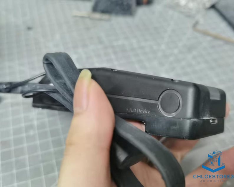 May include: A black 3D printer filament spool holder with a black rubber strap. The holder has a label that reads "S.I.I.P Device".