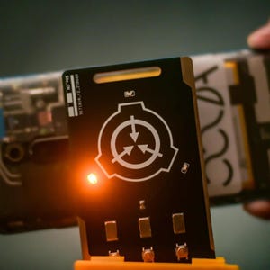 May include: A rectangular black access card featuring a white circular logo with three inward-pointing arrows. The card includes a glowing orange LED light, metallic contact points at the bottom, and printed text reading Site_CN and 917181A_Y2.250609.