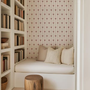 May include: A cozy reading nook with built-in white bookshelves filled with books. A white cushioned bench is adorned with beige pillows, set against a patterned wallpaper. A wooden stool sits in front of the bench.