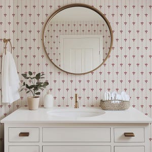 May include: A bathroom vanity with a white countertop, a round gold mirror, and a floral patterned wallpaper. A small potted plant, soap dispenser, and a basket of white towels are on the counter. The faucet and cabinet hardware are gold.