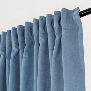 May include: A set of blue curtains hanging from a black curtain pole. The curtains are made of a textured fabric and have a subtle sheen.