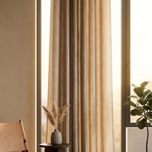 K&ouml;nnte beinhalten: Beige Leinen-Vorh&auml;nge mit &Ouml;sen h&auml;ngen vor einem gro&szlig;en Fenster an einer schwarzen Stange. Ein kleiner Beistelltisch h&auml;lt eine Vase mit getrockneten Pflanzen. Ein Lederstuhl und eine Topfpflanze befinden sich ebenfalls im Raum.