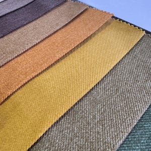 Puede incluir: Una colección de muestras de tela en varios tonos de marrón, naranja, amarillo y verde. La tela tiene una textura ligeramente acanalada.