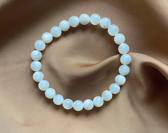 May include: A white pearl bracelet with iridescent beads. The bracelet is made of natural materials and has a simple, elegant design.