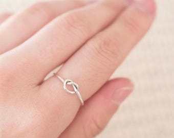 May include: A silver knot ring on a finger.