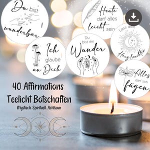 以下が含まれることがあります： 「Du bist wunderbar」や「Ich glaube an Dich」などのフレーズを含む、黒いテキストとイラストが描かれた白い円形のアファメーションのコレクション。画像には、火の灯ったティーライトキャンドルと「40 Affirmations Teelicht Botschaften」の文字も含まれています。