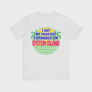 Puede incluir: Una camiseta blanca de manga corta con un gráfico circular que muestra un sol amarillo, palmeras verdes y líneas onduladas. El texto I GOT MY PROSTATE EXAMINED ON EPSTEIN ISLAND aparece en letras azules y rosas en el centro de la prenda.