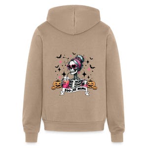 May include: A tan hoodie with a skeleton wearing pink sunglasses and drinking a pink drink. The skeleton is surrounded by bats, stars, and pumpkins. The text "BOO-JEE MAMA" is written on a banner below the skeleton.