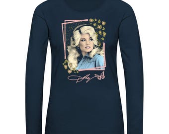 Op de afbeelding: Een marineblauw longsleeve t-shirt met een roze ingelijst beeld van Dolly Parton. De afbeelding heeft een bloemmotief en een vlinder. De tekst "Dolly" staat in roze onder de afbeelding.