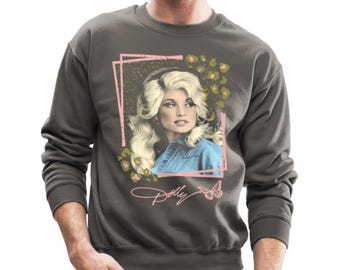 Op de afbeelding: Een antracietkleurig sweatshirt met een vintage afbeelding van Dolly Parton in een blauw denim shirt. De afbeelding is omringd door roze en groene bloemmotieven en een vlinder. De tekst "Dolly" is in een cursief schrift onder de afbeelding geschreven.