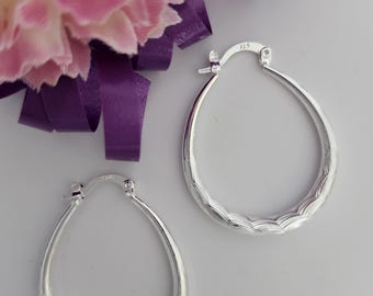 May include: A pair of silver hoop earrings with a textured, wavy design. The earrings are oval shaped and have a hinged closure.