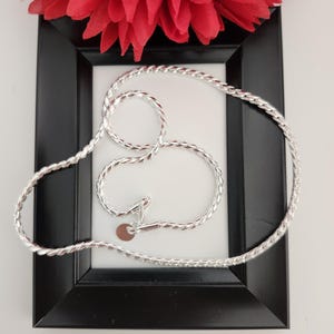 May include: A silver chain necklace with a twisted rope design. The chain is displayed on a black frame against a white background.