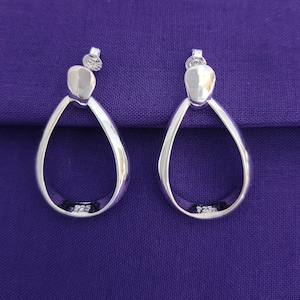 May include: A pair of silver teardrop-shaped earrings with a smooth, polished finish. The earrings have a simple, modern design and are marked with "925" on the back.