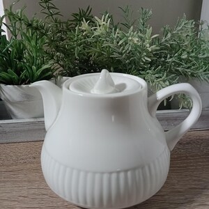 May include: White ceramic teapot with a ribbed design and a lid with a knob. The teapot has a spout and a handle.