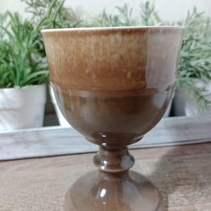 May include: A brown ceramic goblet with a white rim. The goblet has a wide base and a tall, slender stem.