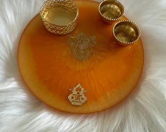 May include: An orange resin tray with gold accents. The tray features a gold filigree candle holder, two small gold candle holders, and gold decorative elements. The tray is set on a white, fluffy surface.