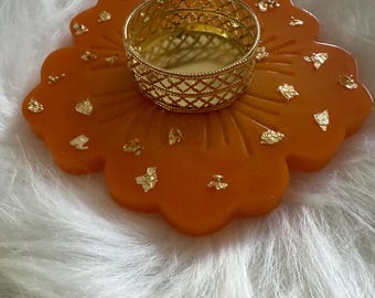 May include: An orange resin candle holder with gold leaf accents and a gold metal lattice cup. The holder is shaped like a flower and is designed to hold a tea light candle. A decorative item for home decor.