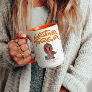 Puede incluir: Taza de cerámica blanca con interior y asa naranja. La taza presenta el texto "Latina Forever" en letras doradas, junto con una ilustración de dibujos animados de una mujer. La taza también tiene el texto "Colombiana Est. 1985".