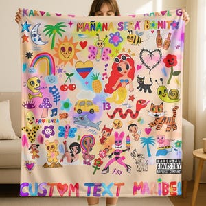 May include: A beige blanket with colorful cartoon illustrations, including a sun, mermaid, and various creatures. Text includes "MAÑANA SERA BONITA" and "CUSTOM TEXT MARIBEL". The blanket has a "Parental Advisory" label.