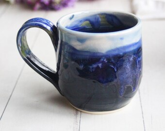 May include: A handmade ceramic mug with a blue and white glaze. The mug has a rounded shape and a handle.