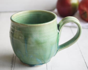 May include: A green ceramic mug with a light green glaze and a crackled finish. The mug has a rounded body and a handle.