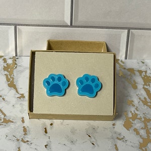 May include: A pair of blue paw print stud earrings in a small cardboard box.