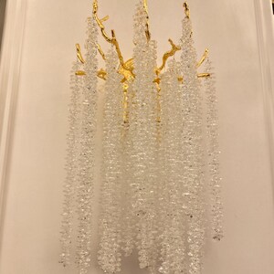 May include: A gold wall sconce with a crystal chandelier design. The sconce features a branch-like structure with cascading crystal strands.