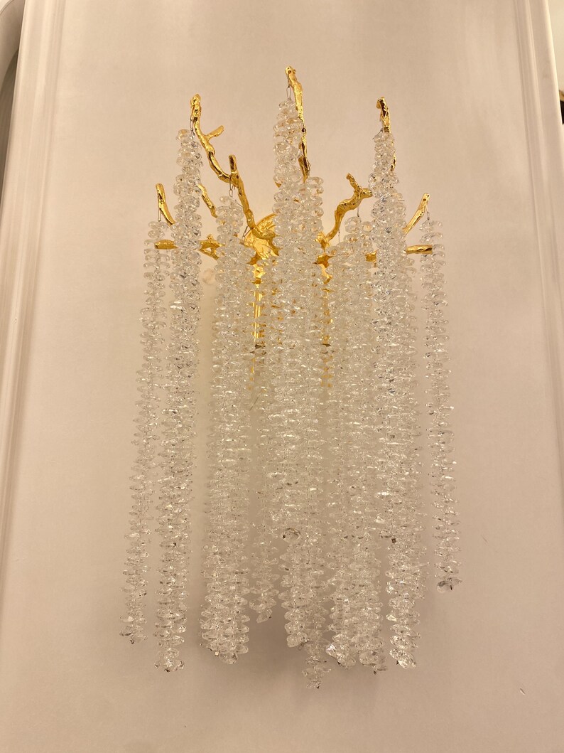 May include: A gold wall sconce with a crystal chandelier design. The sconce features a branch-like structure with cascading crystal strands.