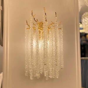 May include: A gold wall sconce with a crystal chandelier design. The sconce features a branch-like frame with cascading crystal beads.
