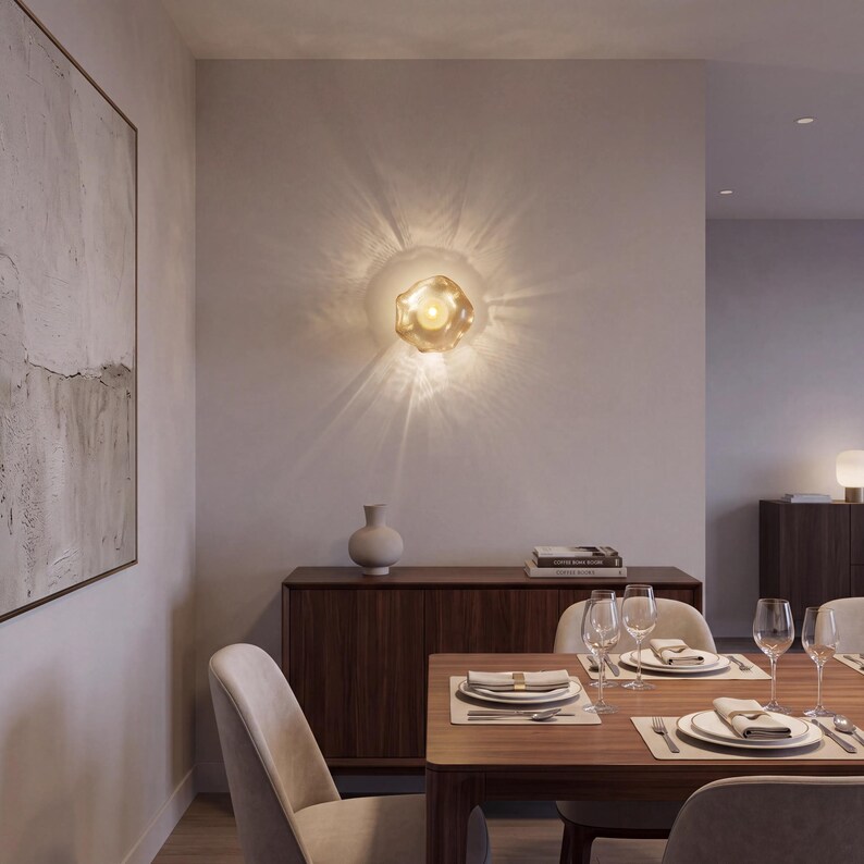 May include: A wall-mounted light fixture with a translucent, organic-shaped glass shade that emits a warm, glowing light, casting distinct, radiating light patterns across the surrounding neutral-toned wall surface.