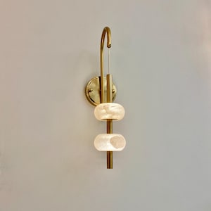 May include: A gold wall sconce with two white, round, frosted glass shades. The sconce has a curved arm and a vertical rod that connects the two shades.