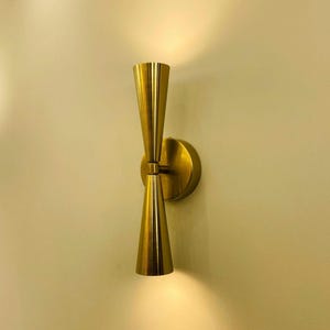 Könnte beinhalten: Eine goldfarbene Wandleuchte mit zwei Leuchten. Die Leuchte hat ein modernes Design mit einer schlanken, minimalistischen Ästhetik.