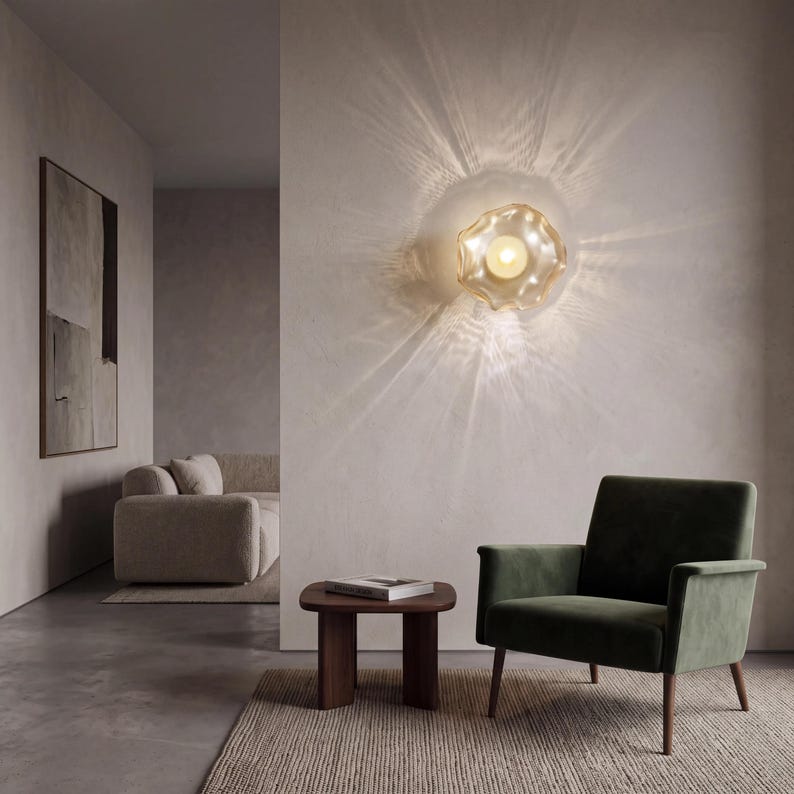 May include: A wall-mounted light fixture featuring a circular, translucent, amber-tinted glass shade with a wavy, organic edge. The light emits a bright, warm glow that casts distinct, radiating light patterns across the wall surface.