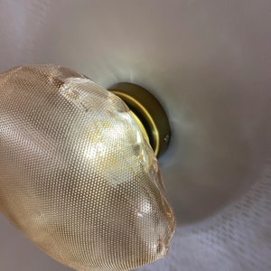 May include: A wall-mounted light fixture featuring a textured, amber-tinted glass shade with a fine dot pattern. The shade is attached to a circular, matte brass-colored metal base that secures the light to the wall surface.