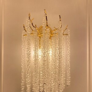 May include: A gold-toned wall sconce with a crystal chandelier design. The sconce features a branch-like structure with cascading crystal beads.