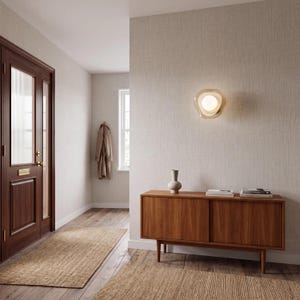 K&ouml;nnte beinhalten: Eine Wandleuchte mit einer kugelf&ouml;rmigen wei&szlig;en Gl&uuml;hbirne, die von einem durchscheinenden, gewellten, bernsteinfarbenen Glasschirm umgeben ist, montiert an einer strukturierten beigen Wand &uuml;ber einem Holzsideboard.