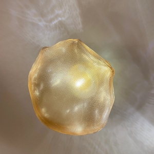 May include: A glowing, spherical pendant light fixture featuring a fine, gold-toned metallic mesh exterior. The light emits a warm, diffused radiance, casting soft, intricate patterns of light and shadow onto the surrounding area.