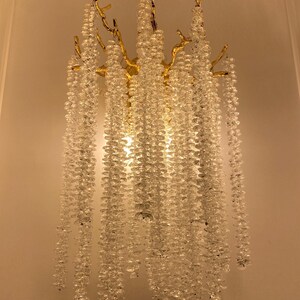 May include: A gold wall sconce with a tree branch design and crystal beads hanging down. The sconce is lit and the beads are reflecting the light.