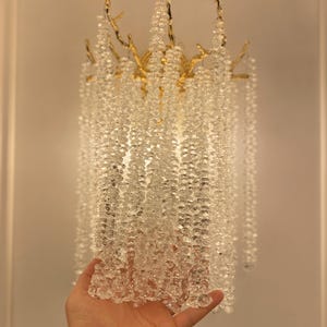 May include: A gold-toned metal chandelier with clear crystal beads hanging from the branches. The chandelier is designed to look like a tree with branches and leaves.