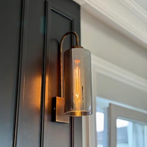 May include: A white ceramic mug with a black handle and the text "But First, Coffee" in a bold, black font. The mug is set against a blurred background, suggesting a cozy setting.