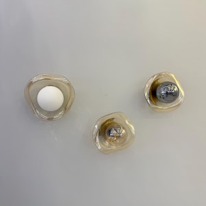 K&ouml;nnte beinhalten: Drei Wandleuchten mit unregelm&auml;&szlig;ig geformten, transparenten, bernsteinfarbenen Glasschirmen. Eine Leuchte enth&auml;lt eine mattwei&szlig;e Kugellampe, w&auml;hrend die anderen beiden kleinere, reflektierende, metallisch silberne Kugellampen enthalten.