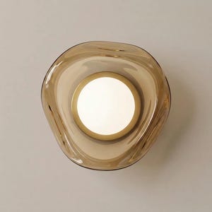 K&ouml;nnte beinhalten: Eine Draufsicht auf eine durchscheinende bernsteinfarbene Glasschale mit einem unregelm&auml;&szlig;igen, organischen, gewellten Rand. Die Mitte der Schale weist einen kreisf&ouml;rmigen, undurchsichtigen wei&szlig;en Boden auf, der ein helles, leuchtendes Erscheinungsbild erzeugt.