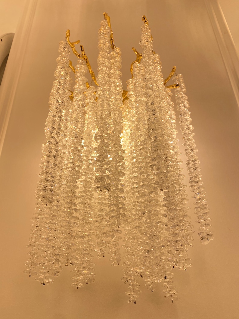May include: A gold-toned metal wall sconce with cascading crystal beads. The sconce has a unique branch-like design and features a cluster of clear crystal beads hanging from each branch.