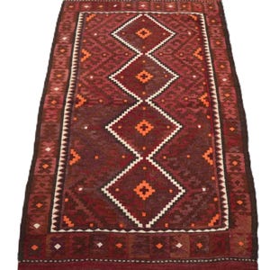 Pode incluir: Um tapete tradicional vermelho, laranja e branco com um padrão de diamantes. O tapete tem uma borda de franjas.