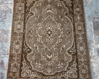 Puede incluir: Una alfombra rectangular marrón con un patrón ornamentado y simétrico. La alfombra presenta un diseño de medallón central rodeado de motivos florales y geométricos en tonos marrones y crema. La alfombra tiene un borde con flecos.