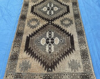 Puede incluir: Una alfombra rectangular con un patrón geométrico en tonos marrón, gris y beige. El diseño presenta formas de diamante y motivos florales. La alfombra probablemente está hecha de material tejido y es adecuada para una sala de estar o dormitorio.