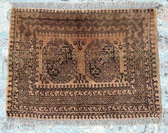 Puede incluir: Una alfombra rectangular anudada a mano con un diseño geométrico marrón y negro. La alfombra presenta un patrón central con dos formas estilizadas y bordes intrincados. Los bordes están acabados con flecos.